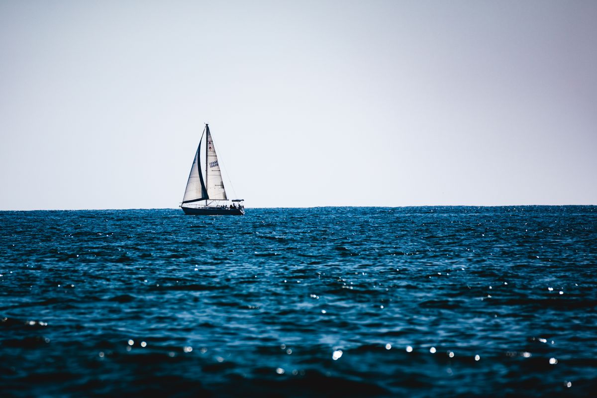 A sailboat at anchor on blue water beside a beach